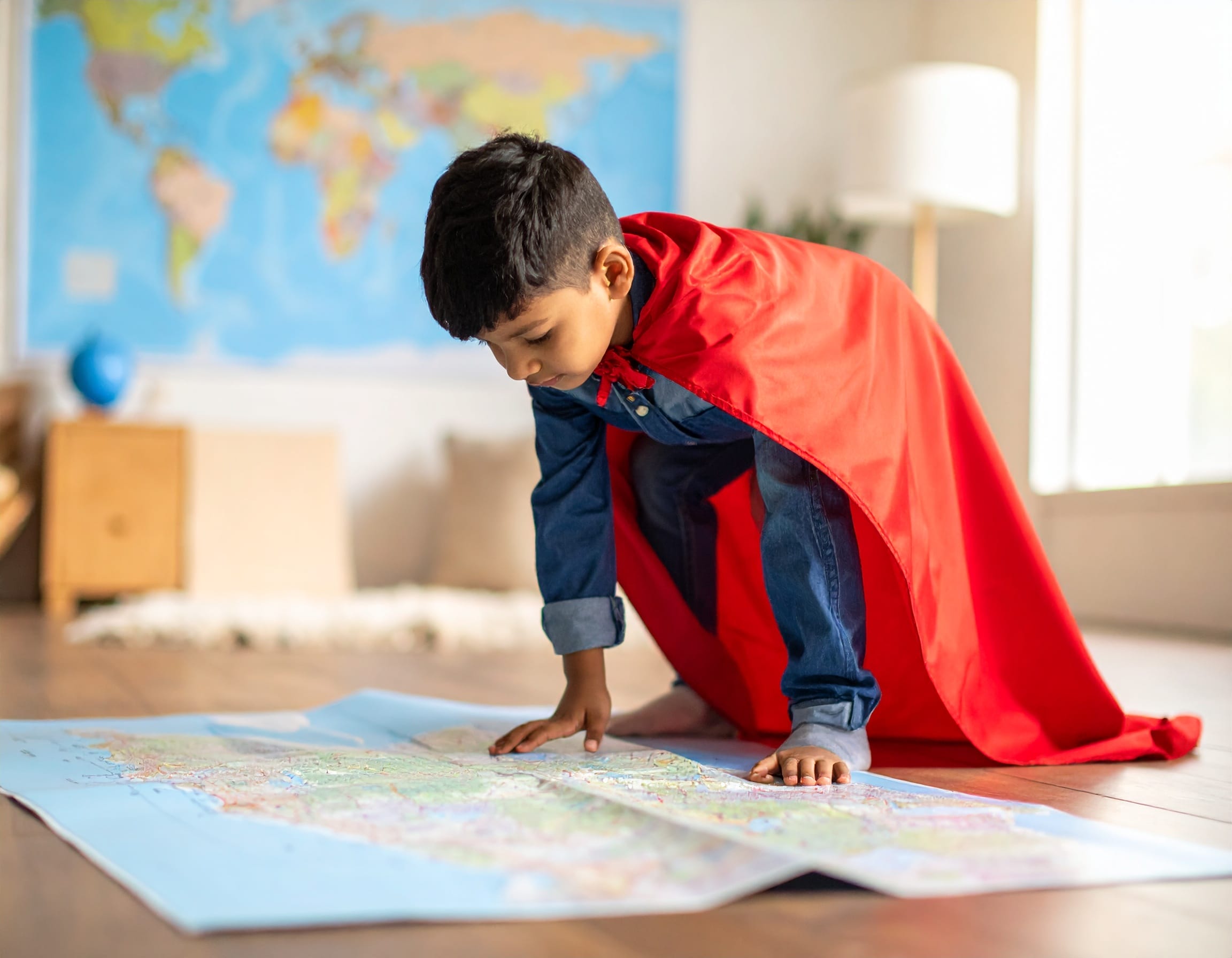 Ein kleiner Junge, der mit einem Superhelden-Cape in einem Raum steht. 